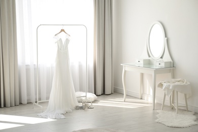 Photo of Beautiful wedding dress hanging on clothing rack in room