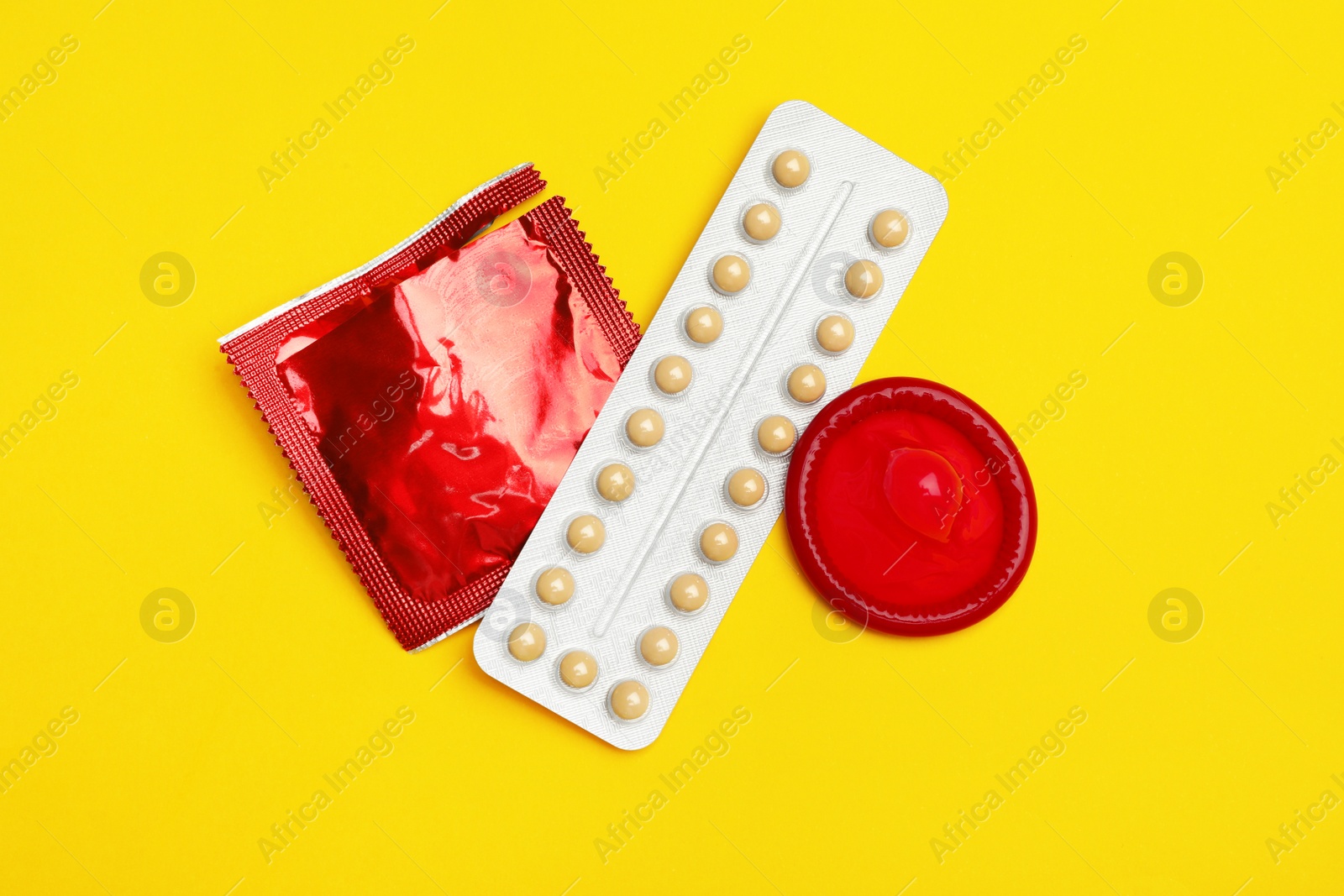 Photo of Condoms and birth control pills on yellow background, flat lay. Safe sex concept