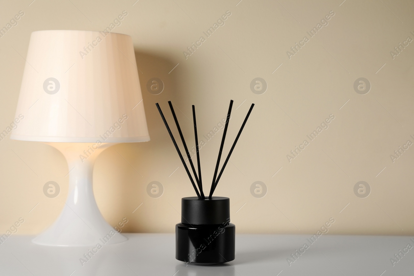 Photo of Aromatic reed air freshener and lamp on white table indoors. Space for text