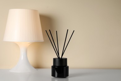 Photo of Aromatic reed air freshener and lamp on white table indoors. Space for text