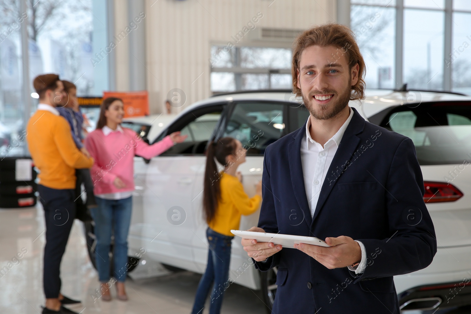 Photo of Car salesman with tablet and blurred family near auto on background