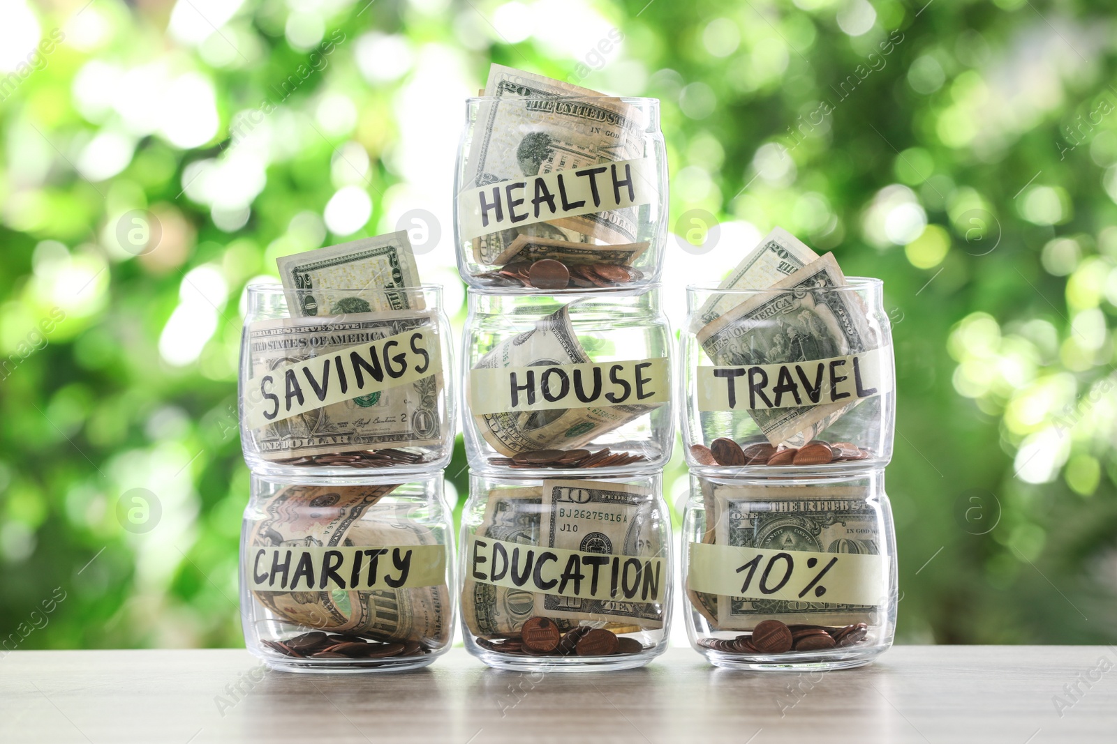 Photo of Glass jars with money for different needs on table against blurred background