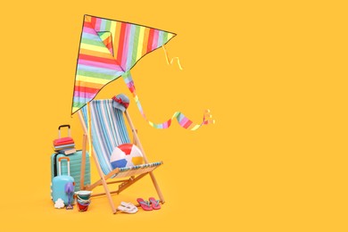 Deck chair, kite, suitcases and beach accessories against orange background, space for text. Summer vacation