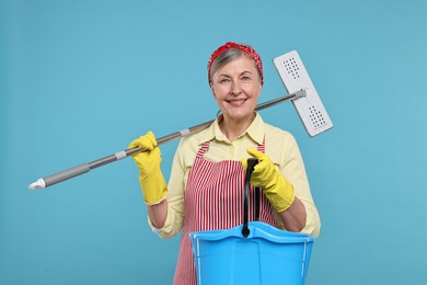 Happy housewife with mop and bucket on light blue background