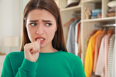 Photo of Young woman biting her nails at home. Space for text