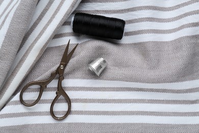 Photo of Thimble, scissors and sewing thread on striped cloth, flat lay. Space for text