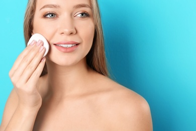 Portrait of beautiful young woman removing makeup with cotton pad on color background