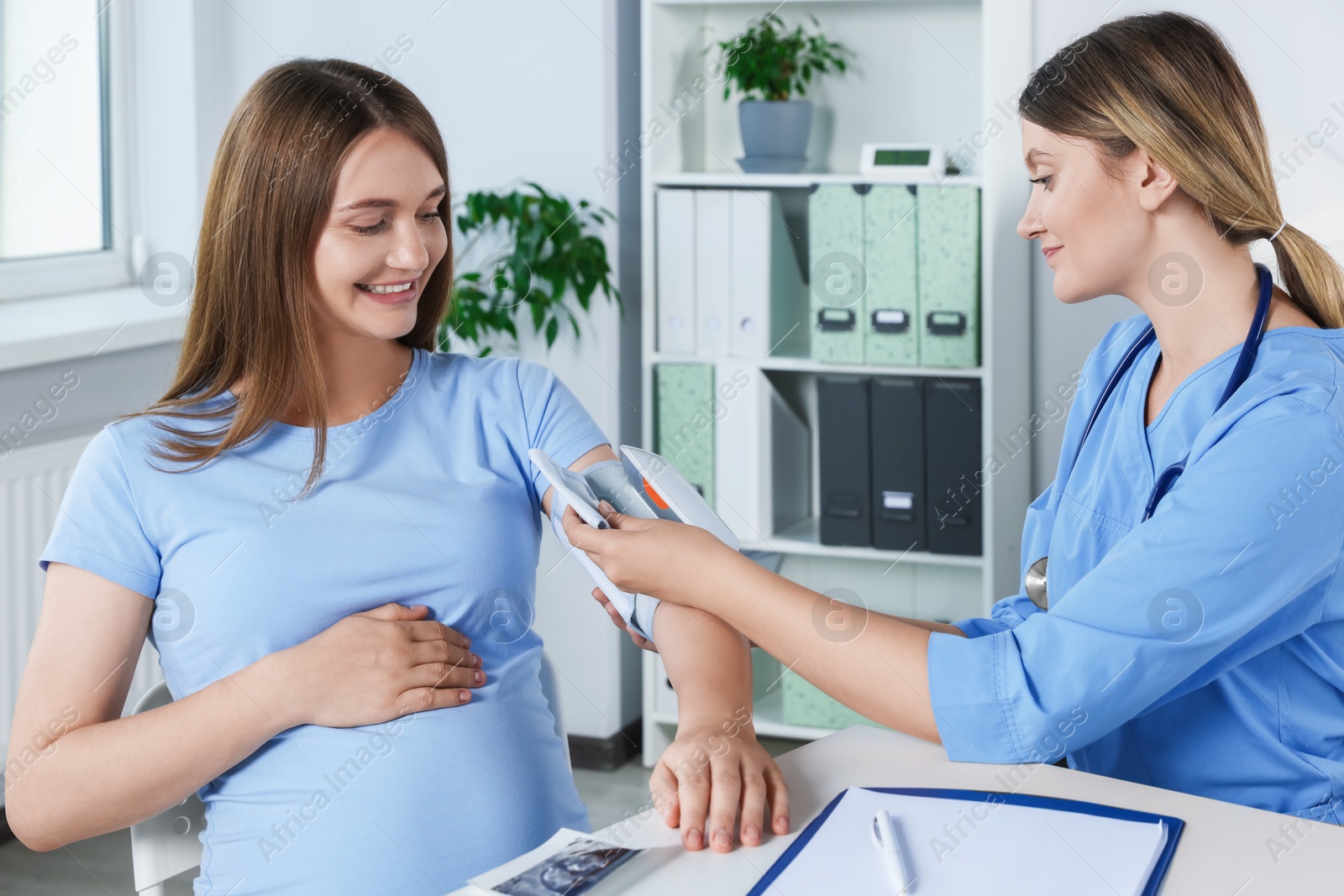 Photo of Doctor measuring blood pressure of happy pregnant woman in hospital