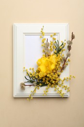 Beautiful floral composition with mimosa flowers and frame on beige background, top view