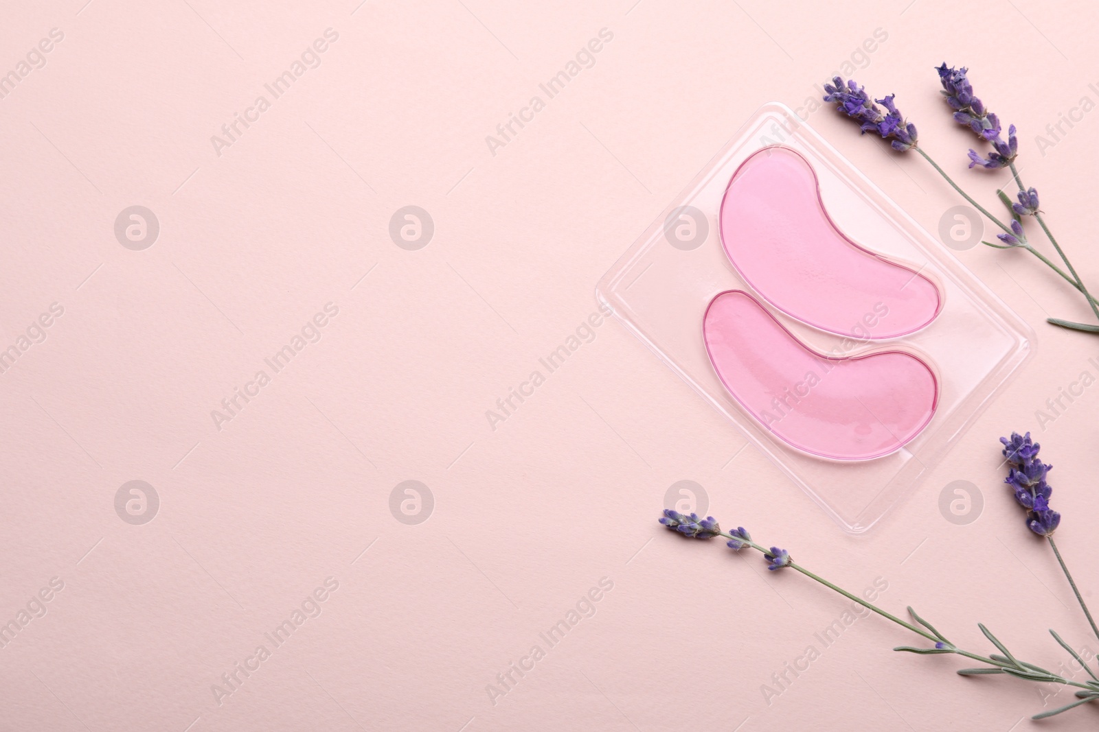 Photo of Package with under eye patches and lavender flowers on light pink background, flat lay. Space for text