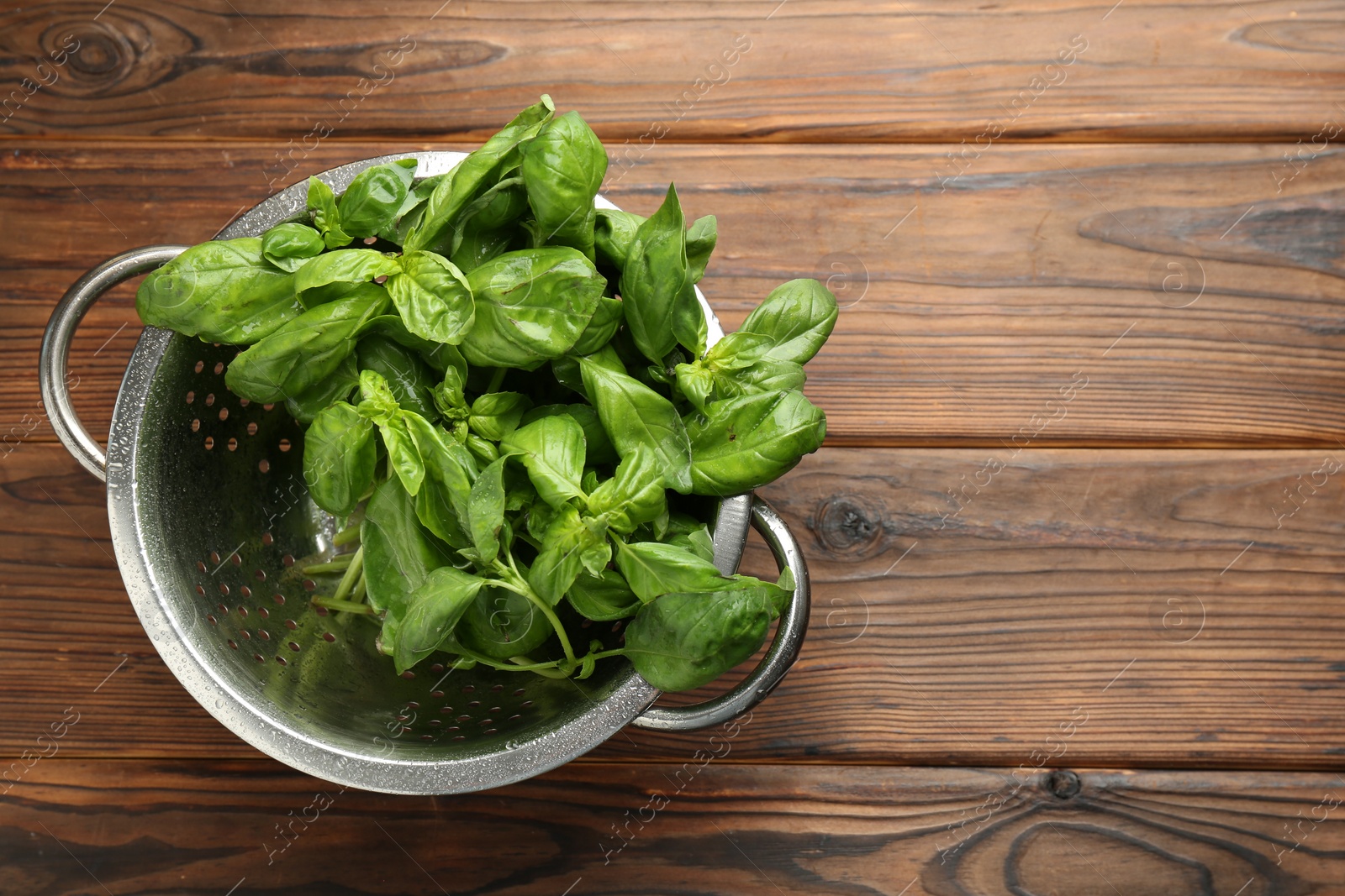 Photo of Metal colander with fresh basil leaves on wooden table, top view. Space for text