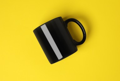 Photo of One black ceramic mug on yellow background, top view