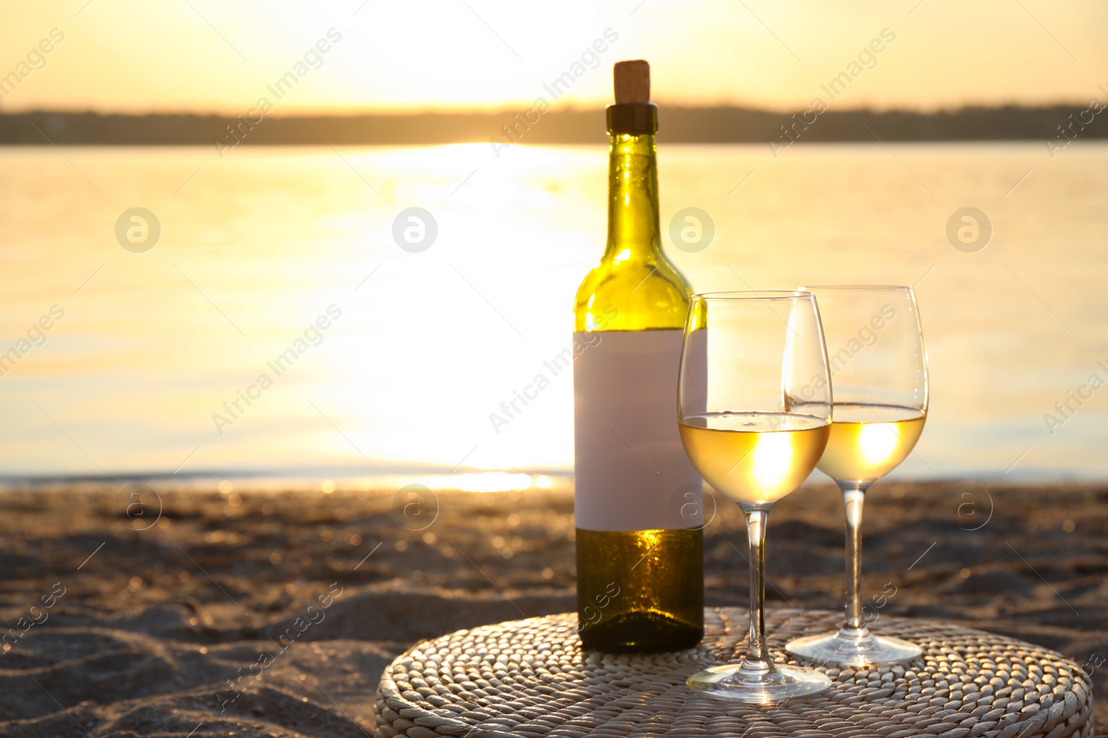 Photo of Bottle and glasses of delicious wine on riverside at sunset