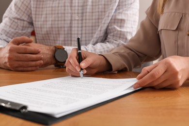 Photo of Businesspeople signing contract at wooden table, closeup of hands