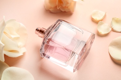 Photo of Bottle of perfume, beautiful flowers and petals on beige background