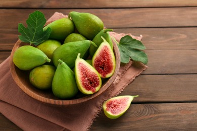 Cut and whole green figs in bowl on wooden table, closeup