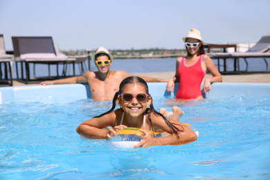 Photo of Happy girl and her parents having fun in swimming pool. Family vacation