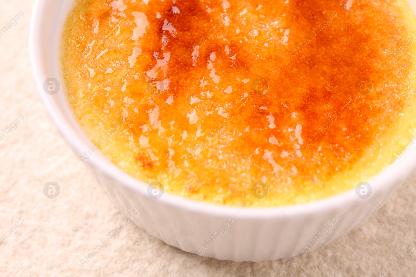 Photo of Delicious creme brulee in bowl on light textured table, closeup