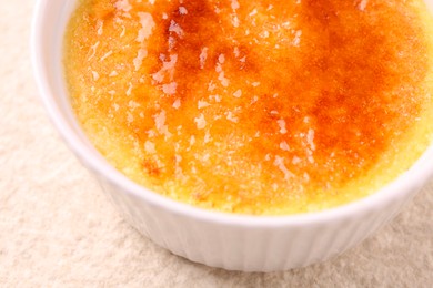 Photo of Delicious creme brulee in bowl on light textured table, closeup