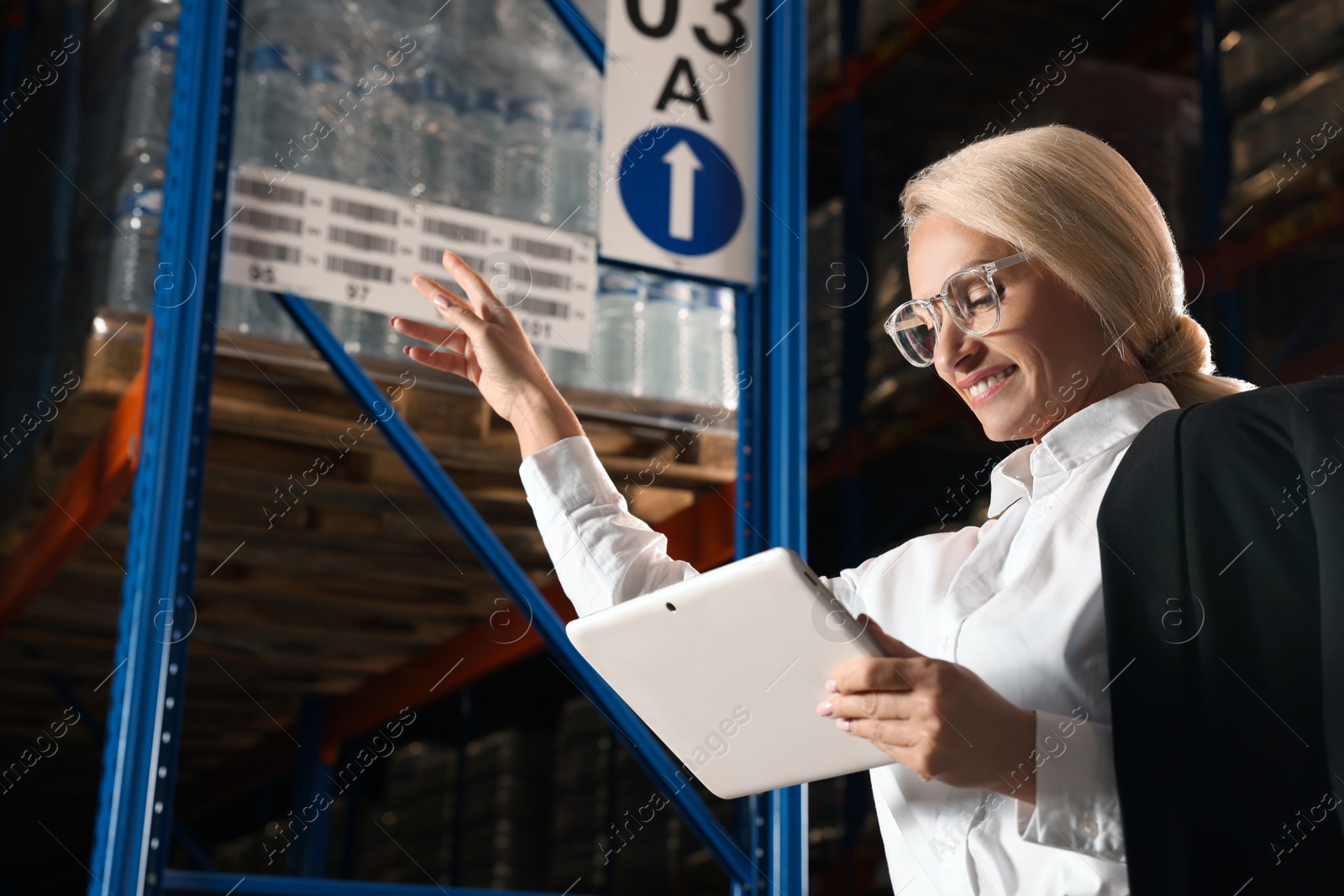 Photo of Happy manager holding modern tablet in warehouse with lots of products. Space for text