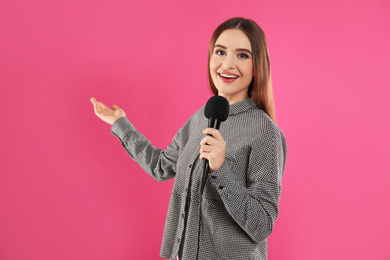 Young female journalist with microphone on pink background