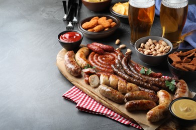 Set of different tasty snacks and beer on dark grey table, space for text