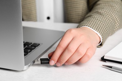 Photo of Woman attaching usb flash drive into laptop at white table, closeup