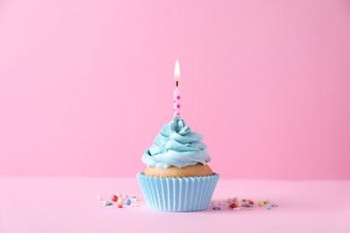 Photo of Delicious birthday cupcake with burning candle and sprinkles on pink background