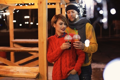 Young couple with cups of mulled wine at winter fair