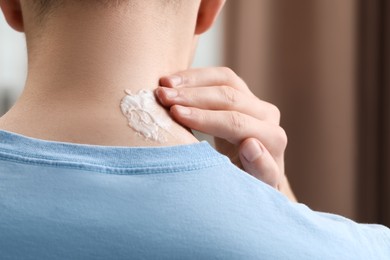Photo of Man applying ointment onto his neck indoors, closeup