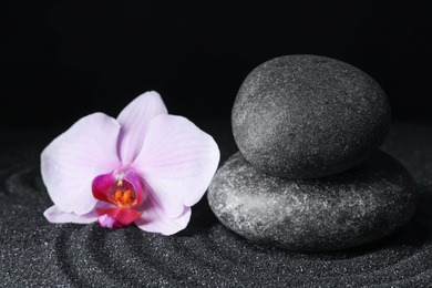 Spa stones and orchid flower on black sand with beautiful pattern. Zen concept