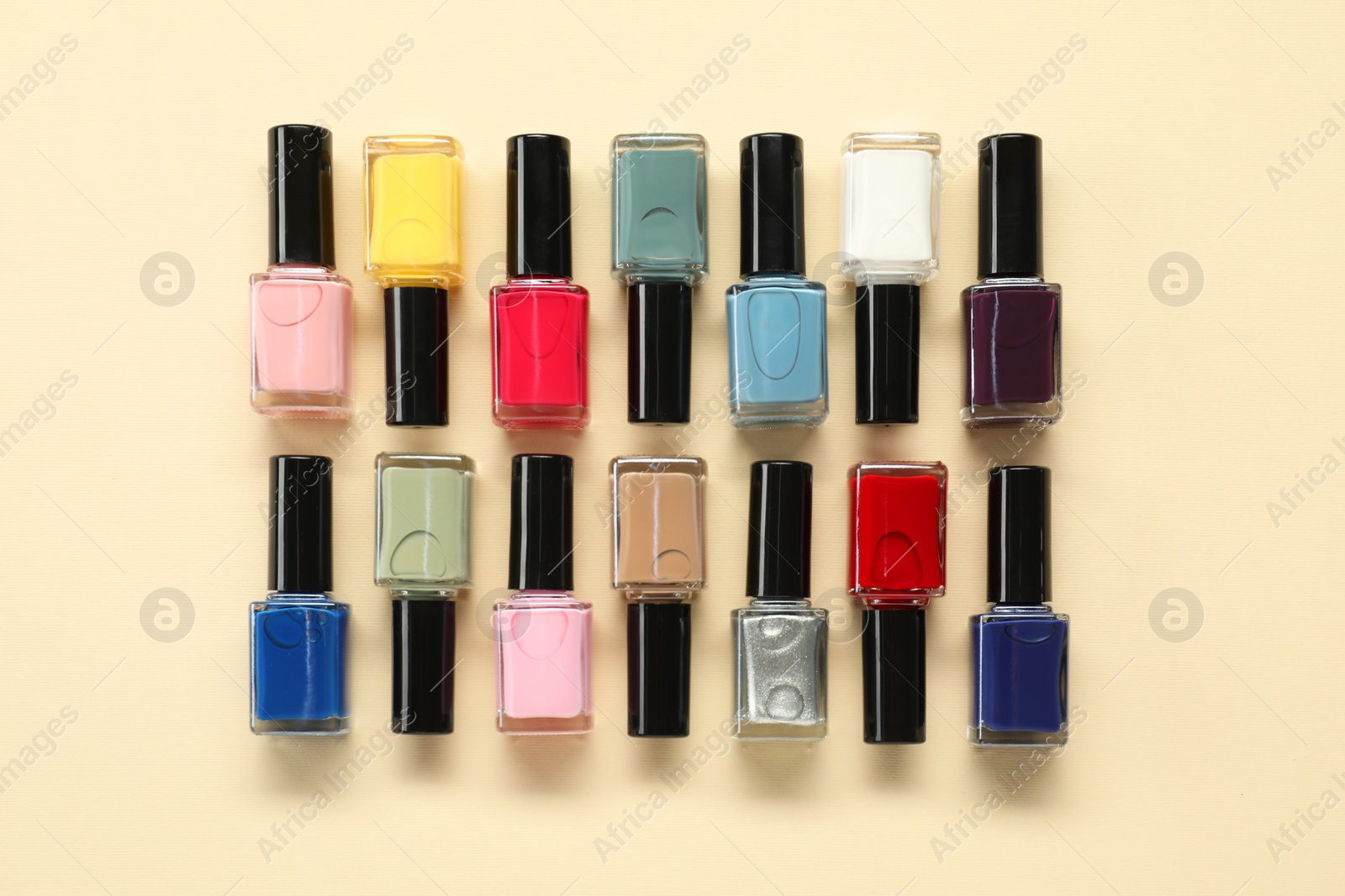 Photo of Bright nail polishes in bottles on beige background, flat lay