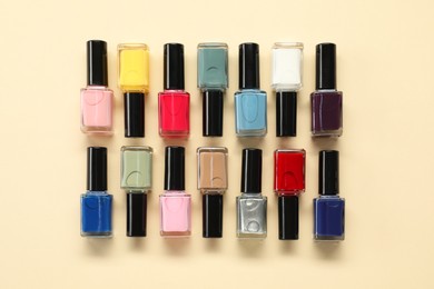 Bright nail polishes in bottles on beige background, flat lay