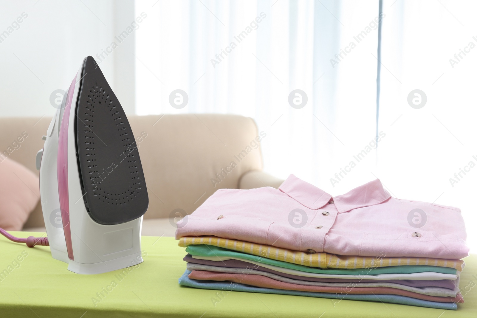 Photo of Board with modern iron and clean laundry at home