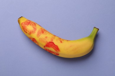 Photo of Banana with red lipstick marks on violet background, top view. Sex concept