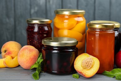 Glass jars with different pickled fruits and jams on grey wooden background