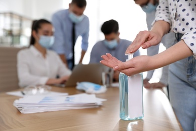 Office worker using hand sanitizer at table, closeup. Personal hygiene during COVID-19 pandemic