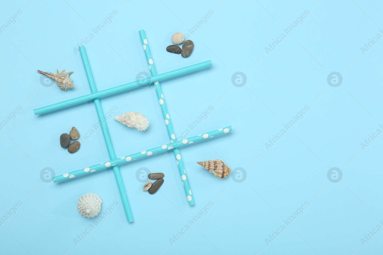 Photo of Tic tac toe game made with sea treasures on light blue background, top view