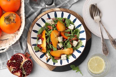 Photo of Tasty salad with persimmon, blue cheese, pomegranate and almonds served on white table, flat lay