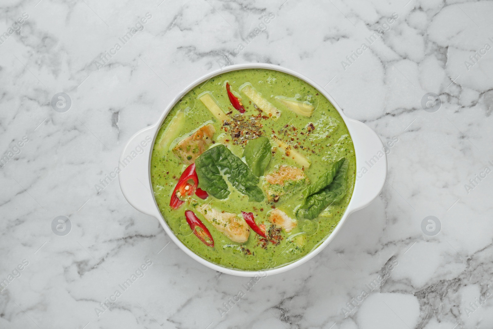 Photo of Saucepan with delicious green curry chicken soup on white marble table, top view