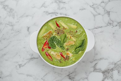 Photo of Saucepan with delicious green curry chicken soup on white marble table, top view