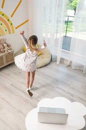 Photo of Cute little girl taking online dance class at home, back view