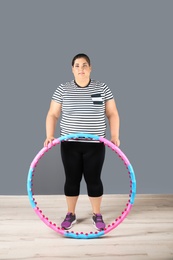 Photo of Overweight woman with hula hoop against gray wall