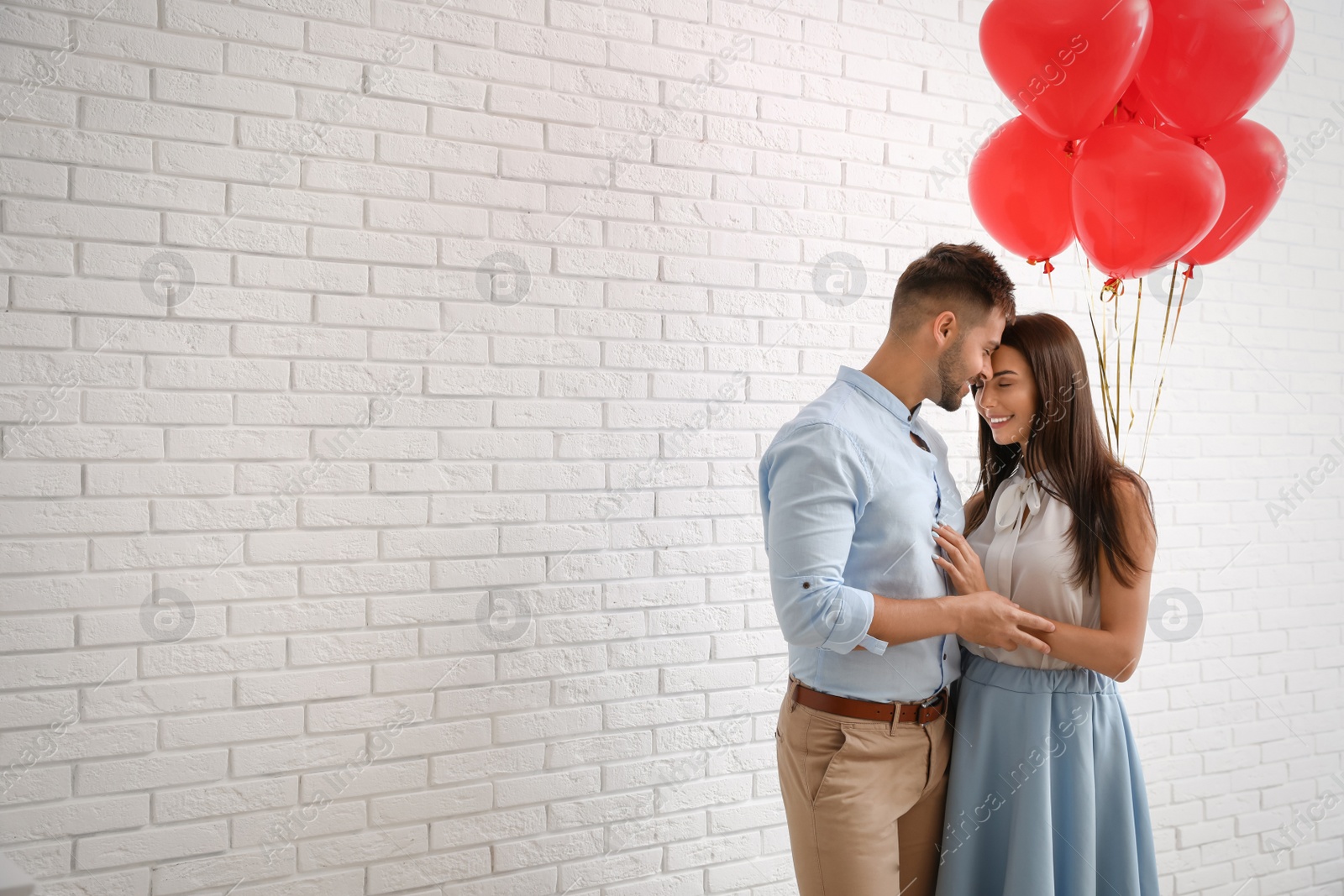 Photo of Young couple with air balloons near white brick wall. Celebration of Saint Valentine's Day