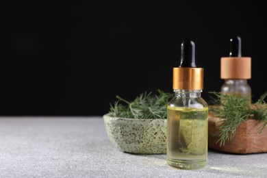 Bottles of essential oil and fresh dill on light grey table, space for text