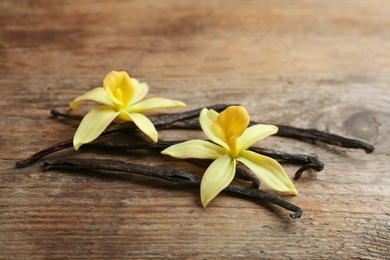 Photo of Vanilla sticks and flowers on wooden background