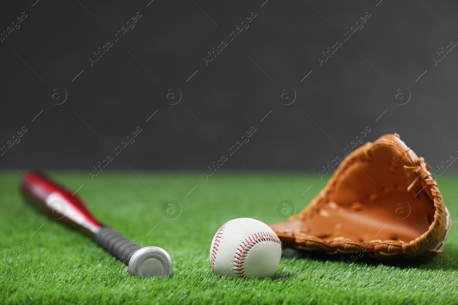 Photo of Baseball bat, leather glove and ball on green grass against dark background. Space for text