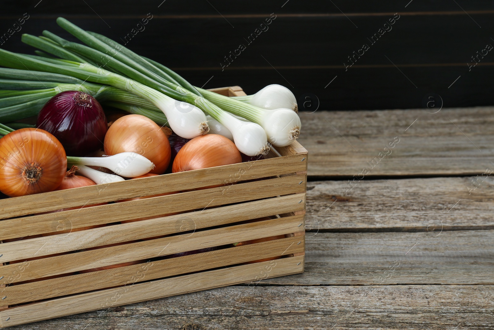 Photo of Crate with different kinds of onions on wooden table, closeup. Space for text