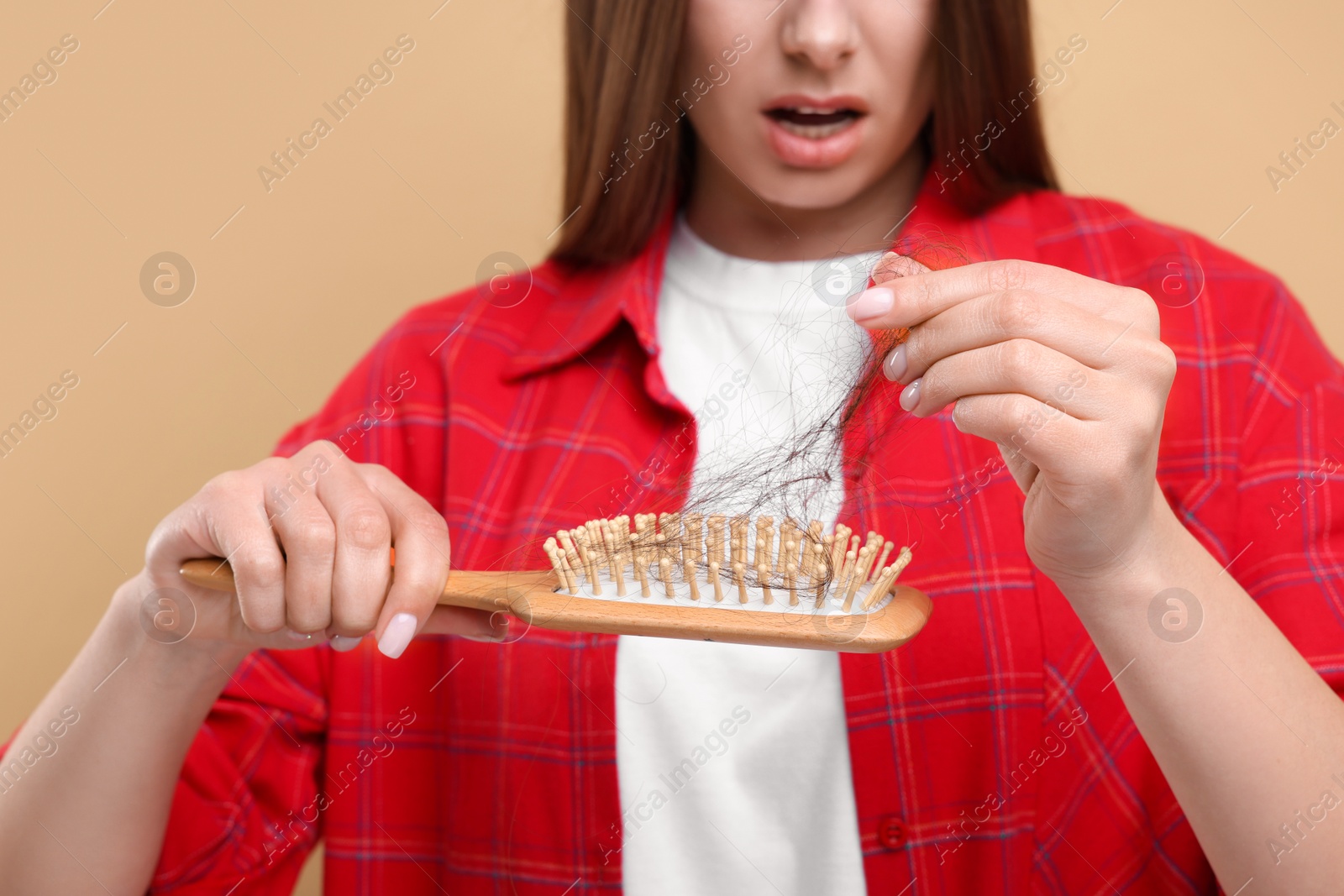 Photo of Woman untangling her lost hair from brush on beige background, closeup. Alopecia problem