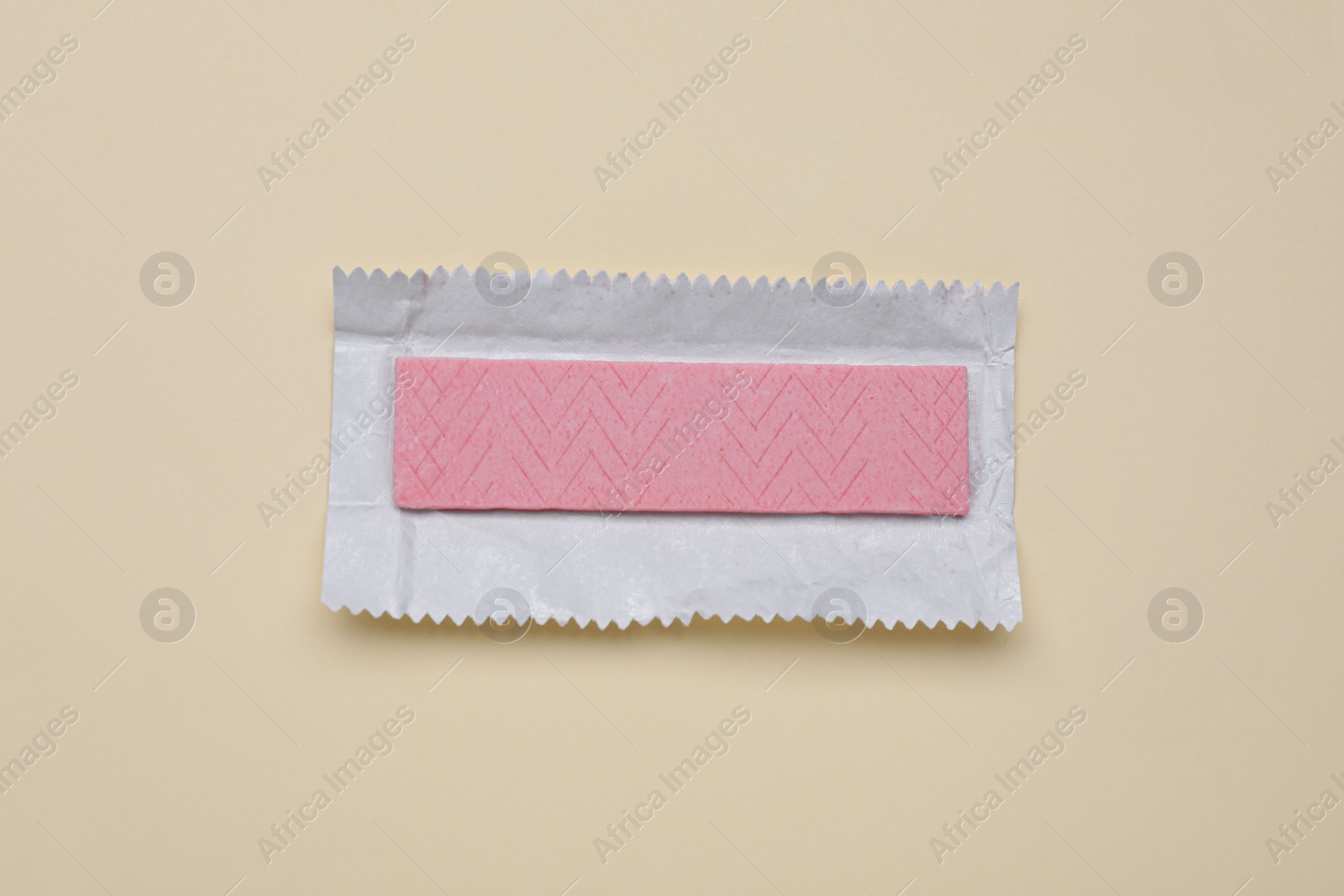 Photo of Unwrapped stick of tasty chewing gum on beige background, top view